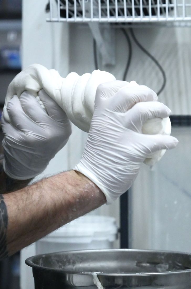 Gloved hands working a batch in the Kind & Co kitchen